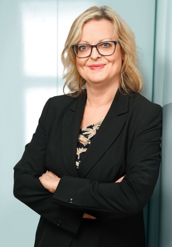 Portrait einer netten Businessfrau mit Brille, die lächelnd vor hellblauem Hintergrund steht